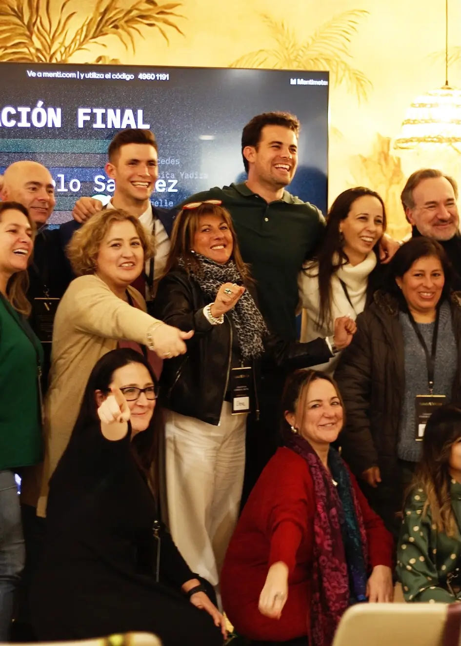 Un grupo de personas sonriendo y posando juntas en un espacio interior frente a una pantalla grande.